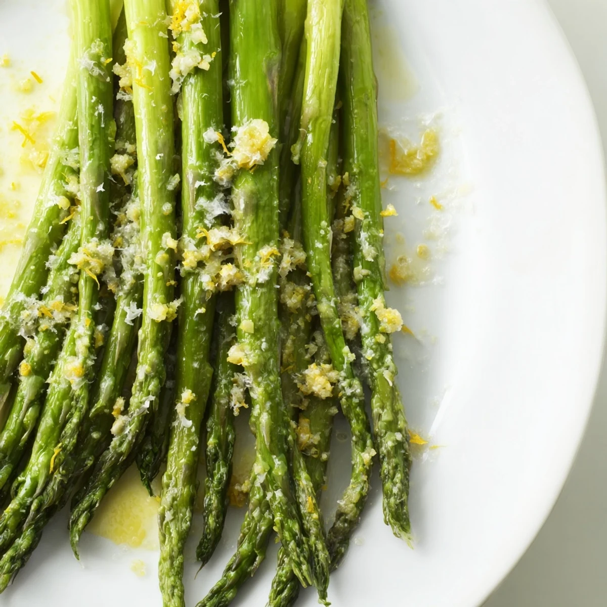 A close-up view of vibrant, tender asparagus coated in olive oil, melted Parmesan, and tangy lemon juice, highlighting its savory Mediterranean flavors.