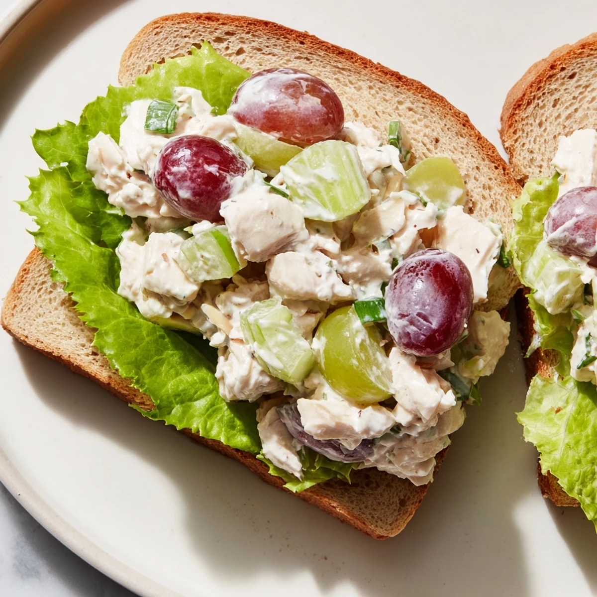 A close-up of a Chicken Salad Sandwich with Grapes on whole wheat bread, featuring creamy dressing, crisp celery, and juicy red grapes.