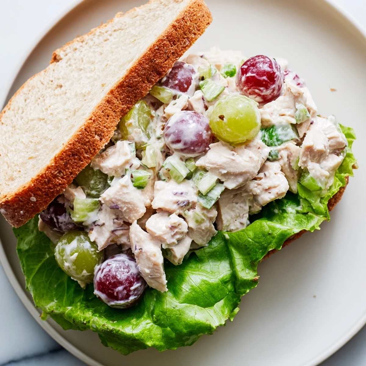 A freshly prepared Chicken Salad Sandwich with Grapes, cut in half to reveal tender chicken, green grapes, and crisp lettuce on sourdough.