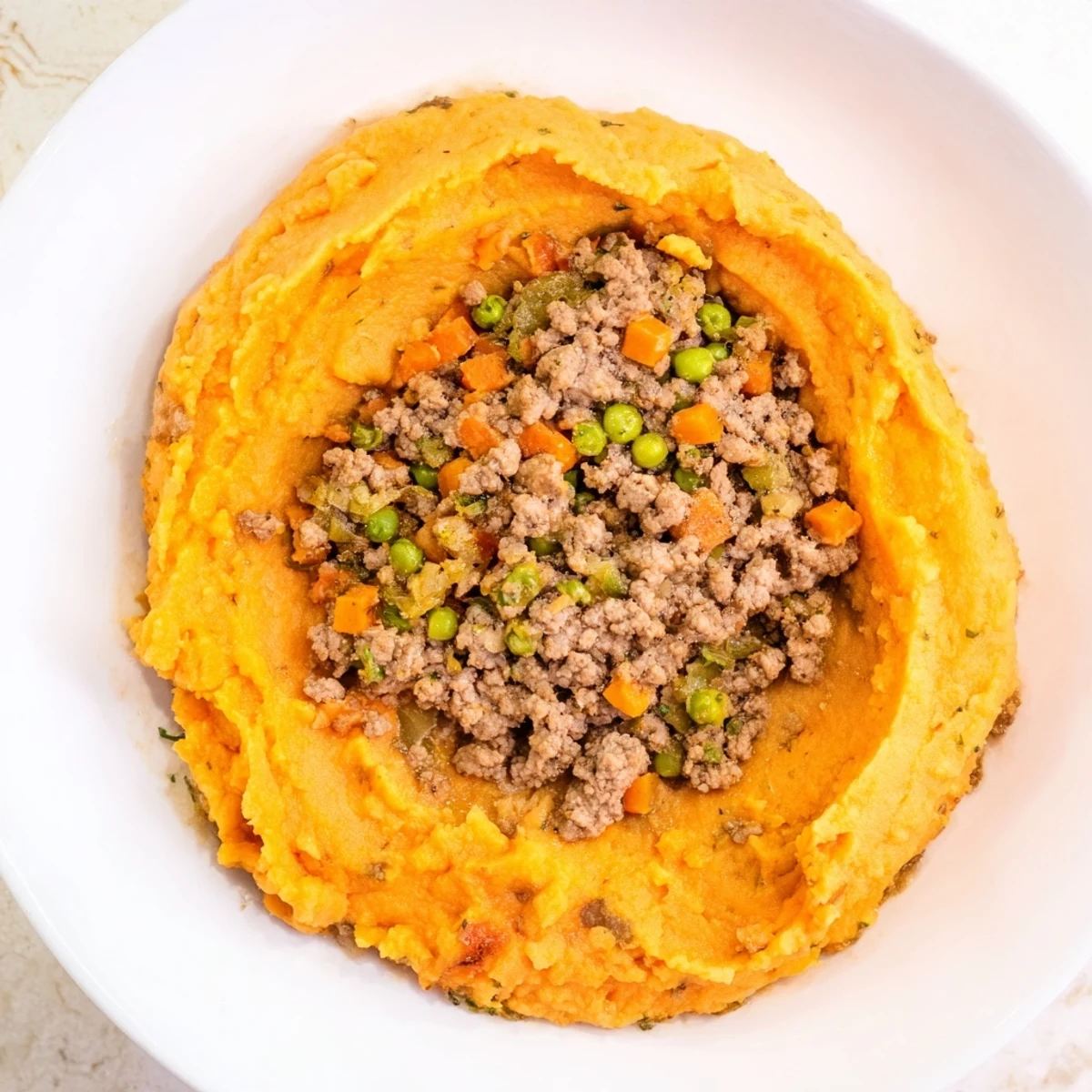 Close-up view of a slice of Beef Shepherds Pie with Sweet Potato, revealing the savory beef filling and smooth, vibrant orange topping.