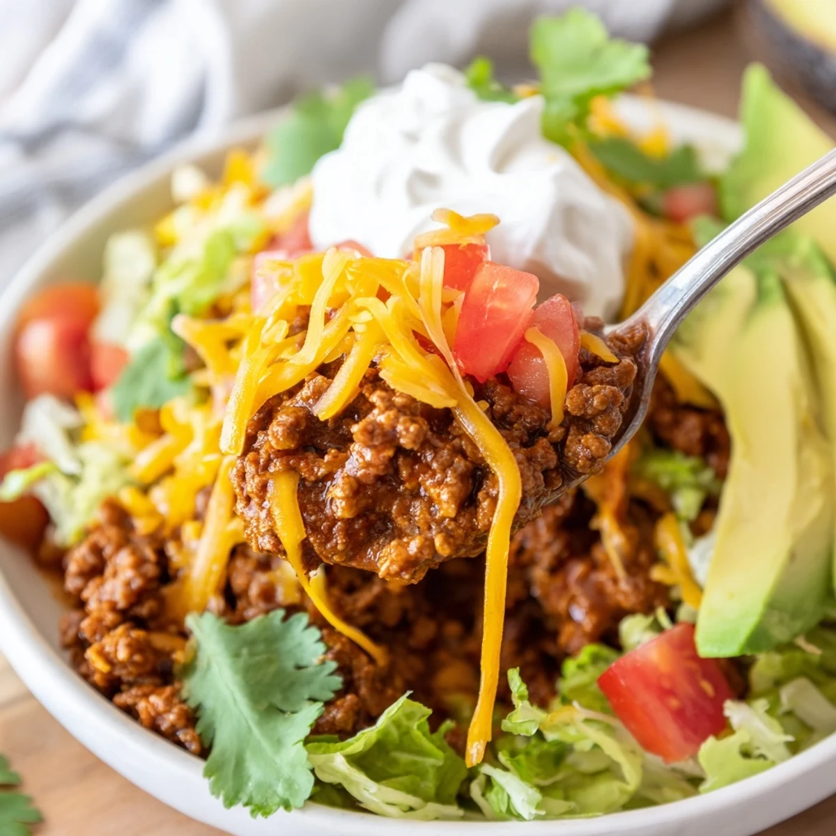 Freshly assembled beef tacos with soft flour tortillas, topped with shredded lettuce, diced tomatoes, cheddar cheese, avocado slices, and a dollop of sour cream.