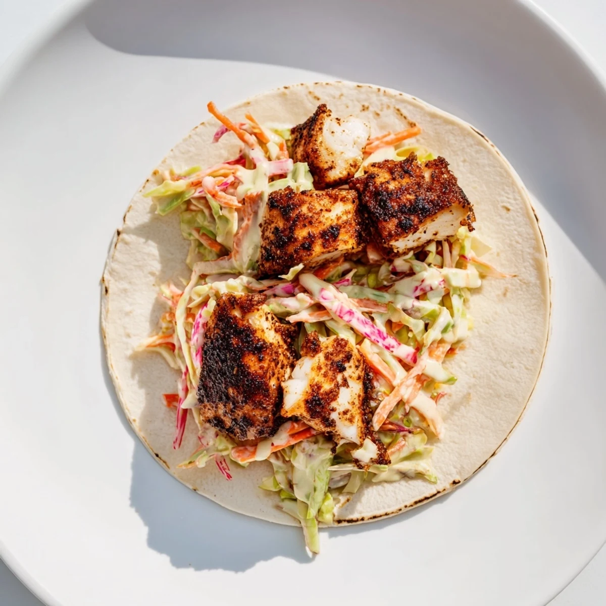 Blackened Fish Tacos with Slaw are garnished with fresh cilantro and lime wedges on a rustic wooden table, ready to serve.