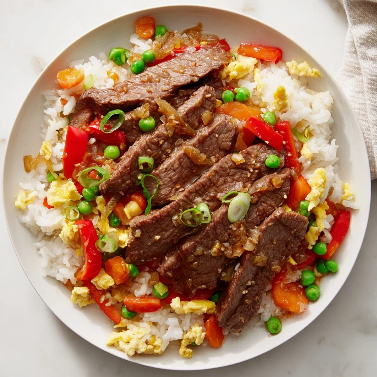 Beef Fried Rice with Vegetables plated in a white bowl includes juicy beef, crisp bell peppers, carrots, and peas, with chopsticks nearby for an easy weeknight Asian-style meal.