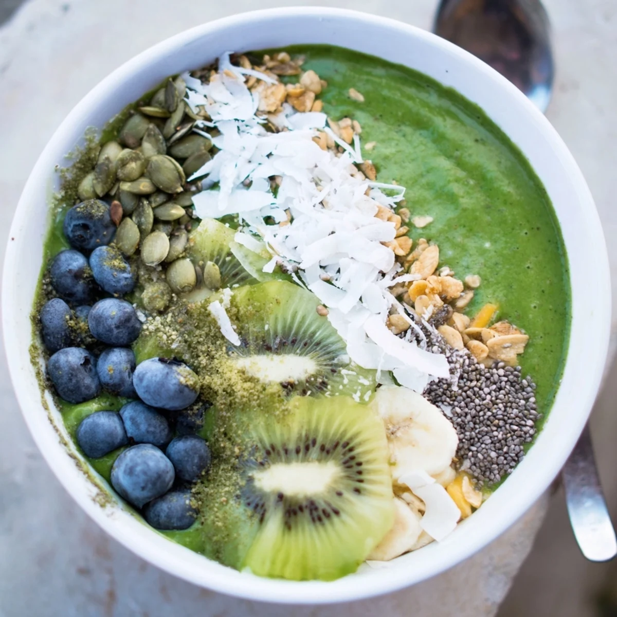A vibrant Green Smoothie Bowl with Toppings is layered with fresh berries, crunchy granola, and creamy avocado slices for a healthy breakfast.