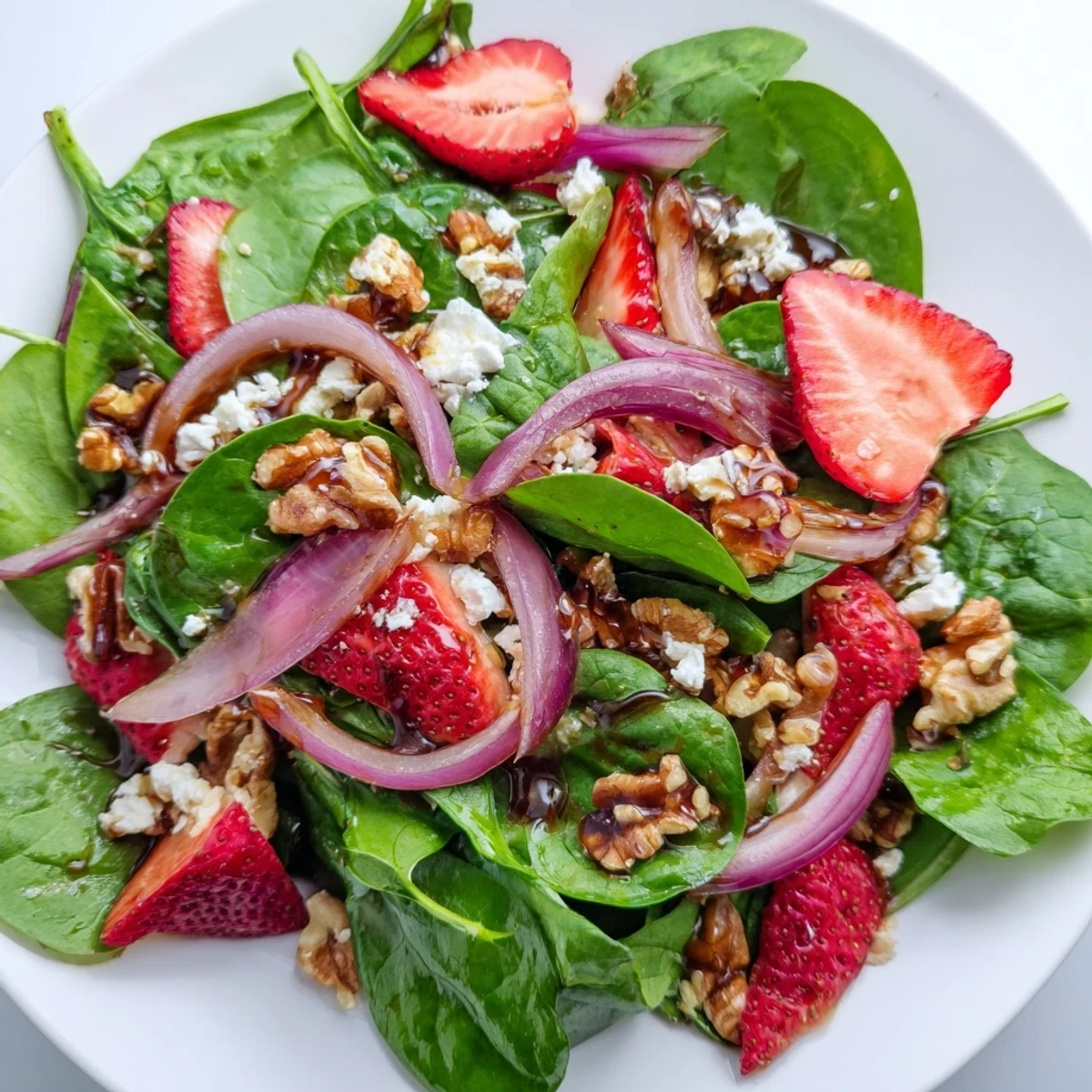 Fresh baby spinach and sliced strawberries topped with crunchy walnuts, crumbled feta, and tangy balsamic vinaigrette in a light summer salad.