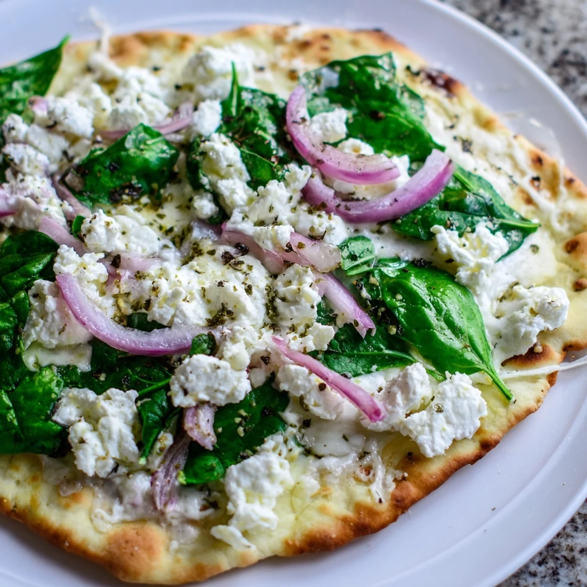 Golden-baked spinach and feta flatbread pizza with melted mozzarella and red onion slices, served on a wooden cutting board.