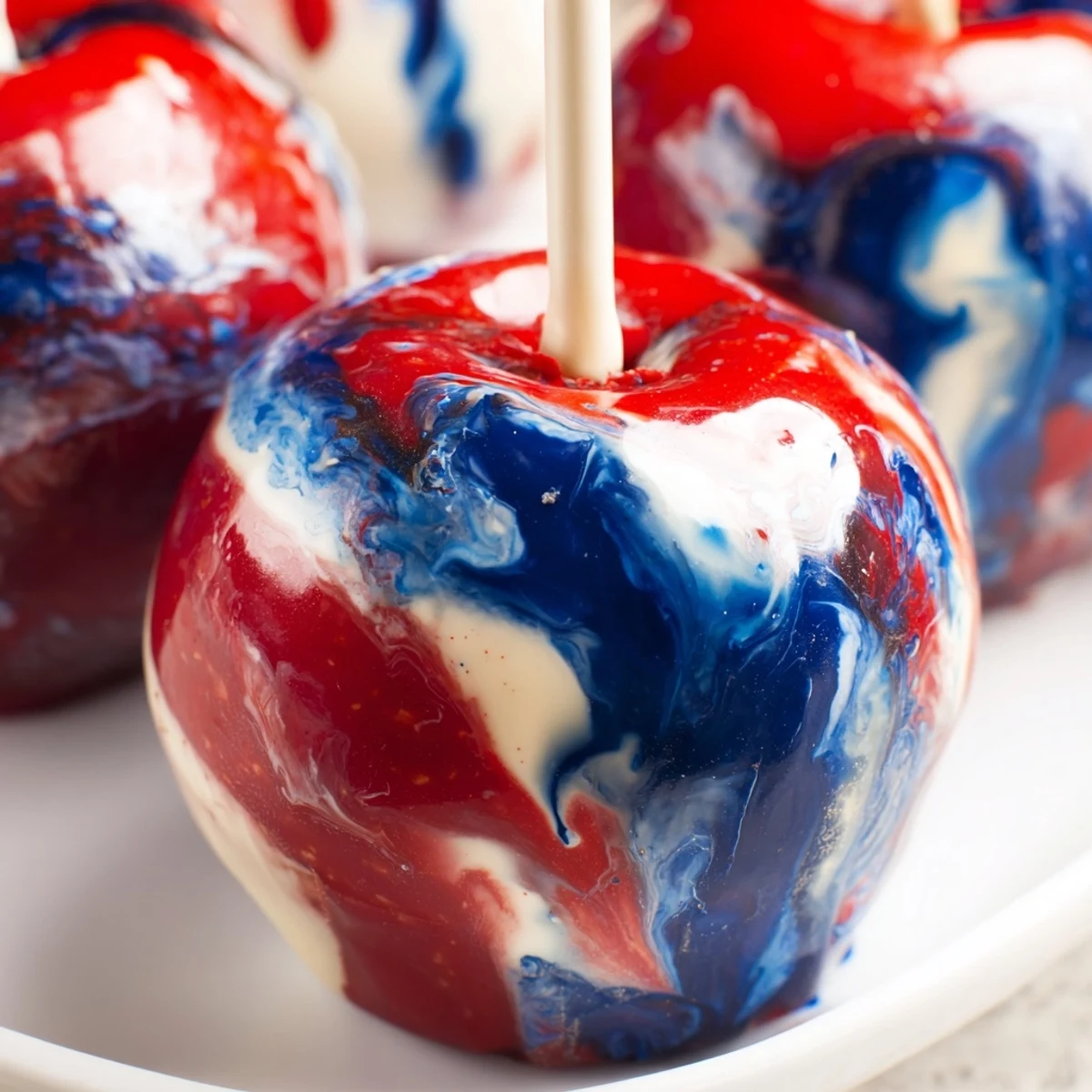 Marbled effect candy apples sitting on a parchment-lined tray with a festive party dessert table backdrop.