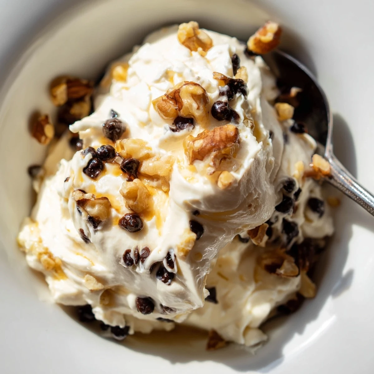A spoon dips into creamy Guilt Free Greek Yogurt Cookie Dough with dark chocolate chips and walnuts on a marble counter.