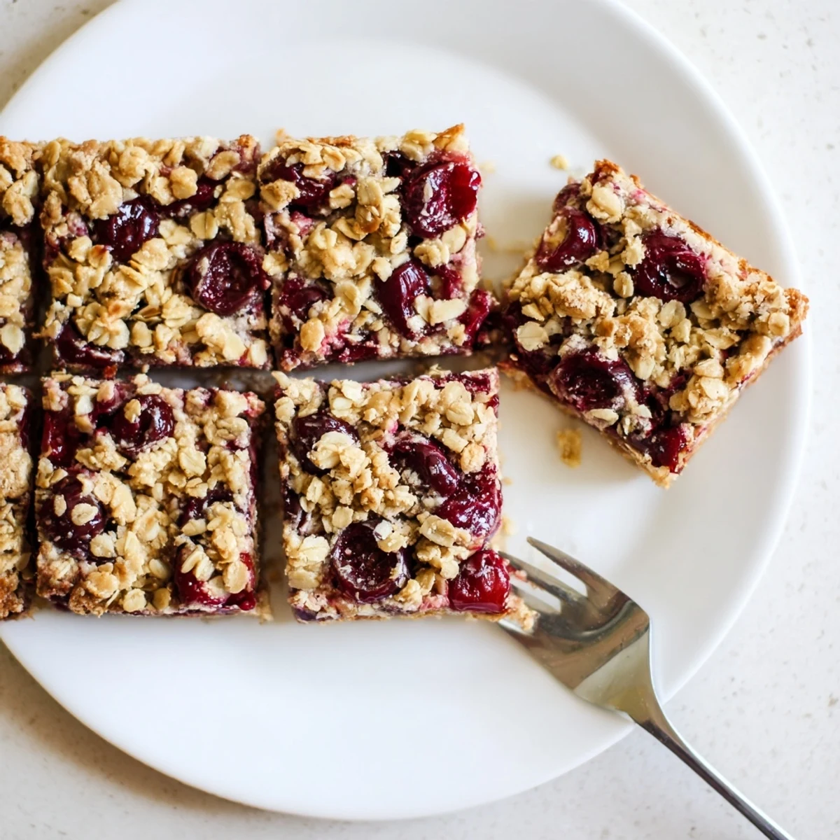 A hand lifting a warm slice of Easy Tasty Cherry Crumble Bars, revealing the buttery crust and bubbly fruit center.