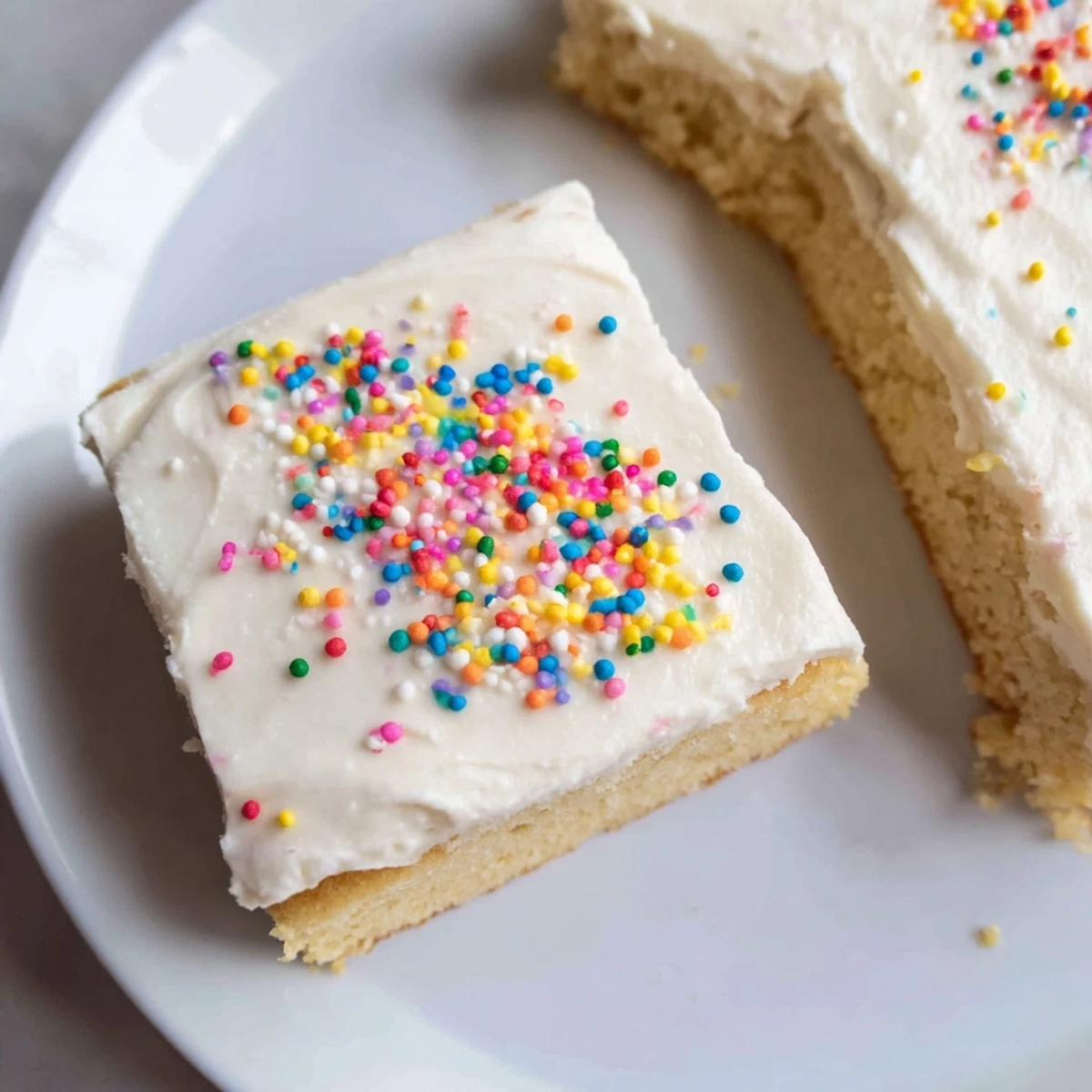 Freshly baked Sugar Cookie Bars with creamy vanilla frosting and colorful sprinkles, cut into neat squares on a white plate.