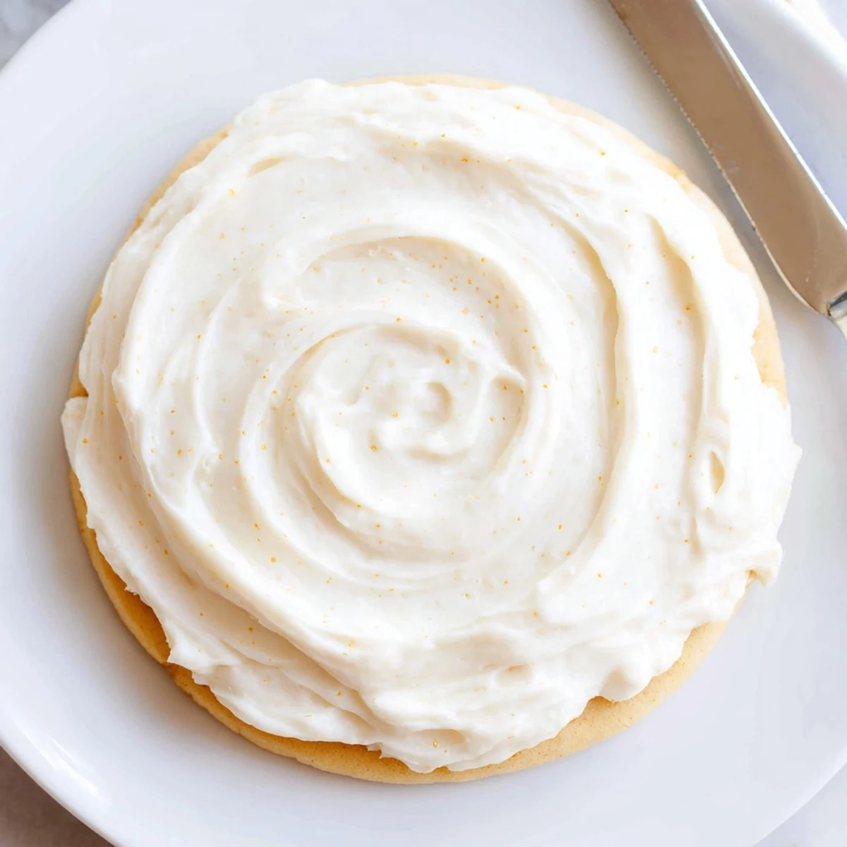 Easy Sugar Cookie Frosting in a bowl next to sugar cookies and a spatula, ready for decorating.