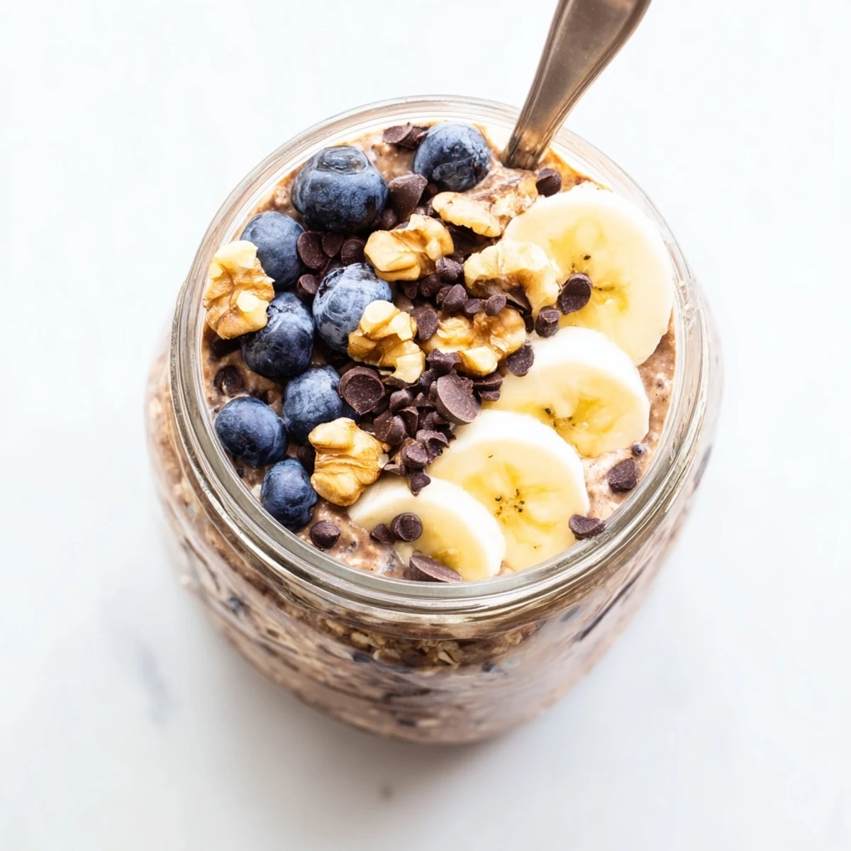 This creamy jar of Ultimate Healthy Chocolate Overnight Oats is topped with sliced banana and walnuts.