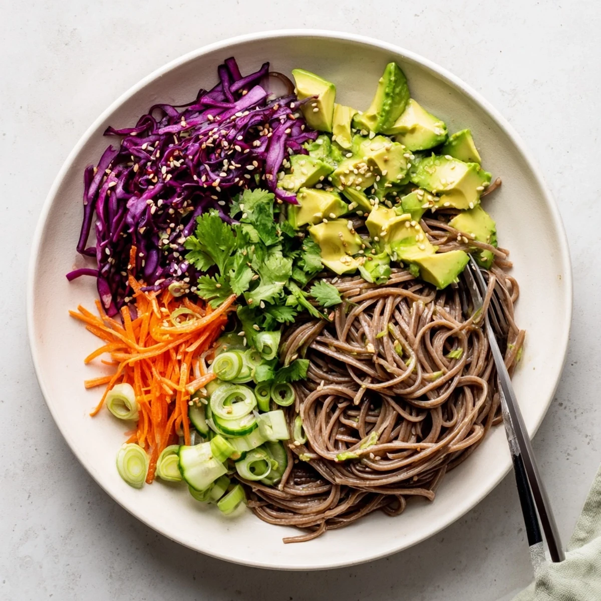 Steamed buckwheat soba noodles tossed with creamy avocado, crisp veggies, and a savory sesame dressing in a bright bowl.