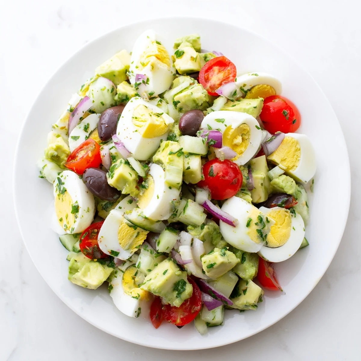 Creamy Mediterranean avocado egg salad with cherry tomatoes, olives, and fresh parsley drizzled with lemon olive oil dressing