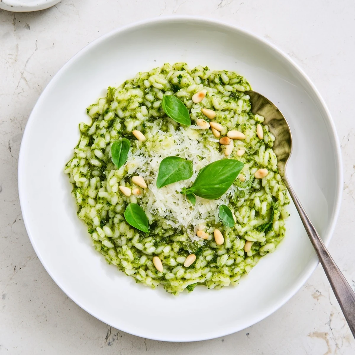 Creamy Parmesan pesto risotto served in a white bowl topped with fresh basil leaves and grated cheese