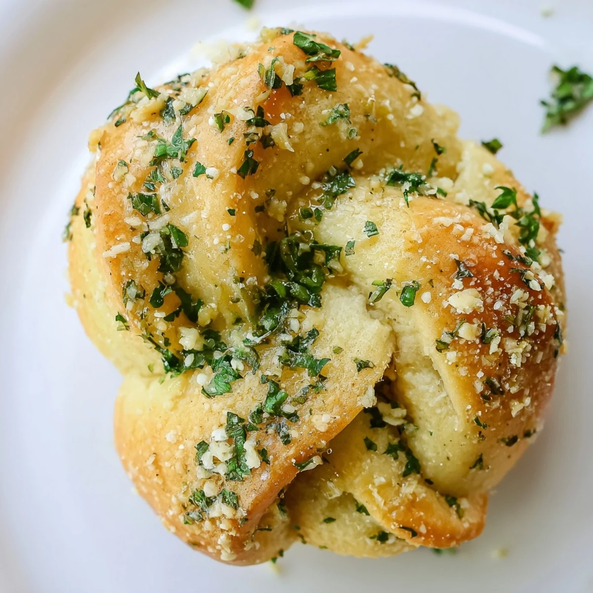 Soft pillowy gluten-free garlic knots arranged on a white plate, garnished with grated Parmesan and chopped green herbs