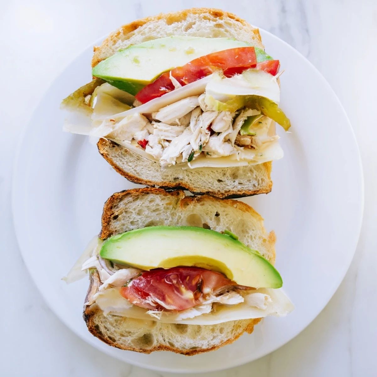 Golden toasted chicken avocado melt sandwich with melted cheese and sliced tomato on a plate