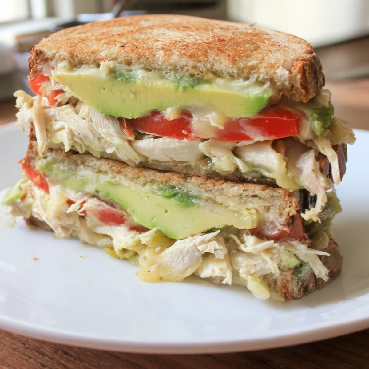 Crispy sourdough chicken avocado melt sandwich oozing melted cheese with fresh avocado slices on top