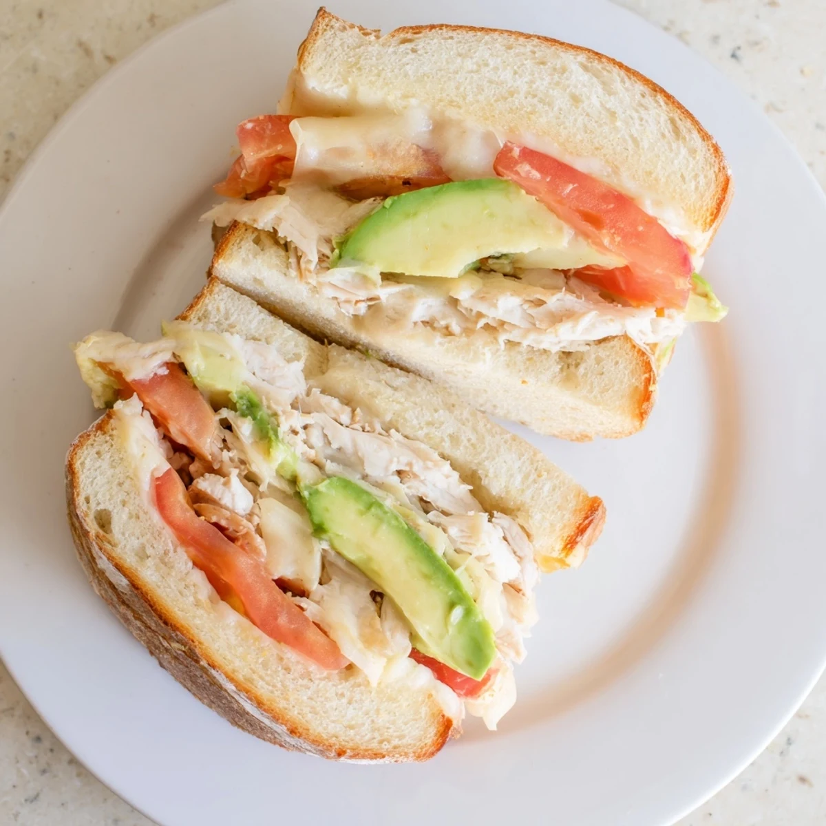 Warm grilled chicken avocado melt sandwich cut in half revealing layers of creamy avocado and melted provolone