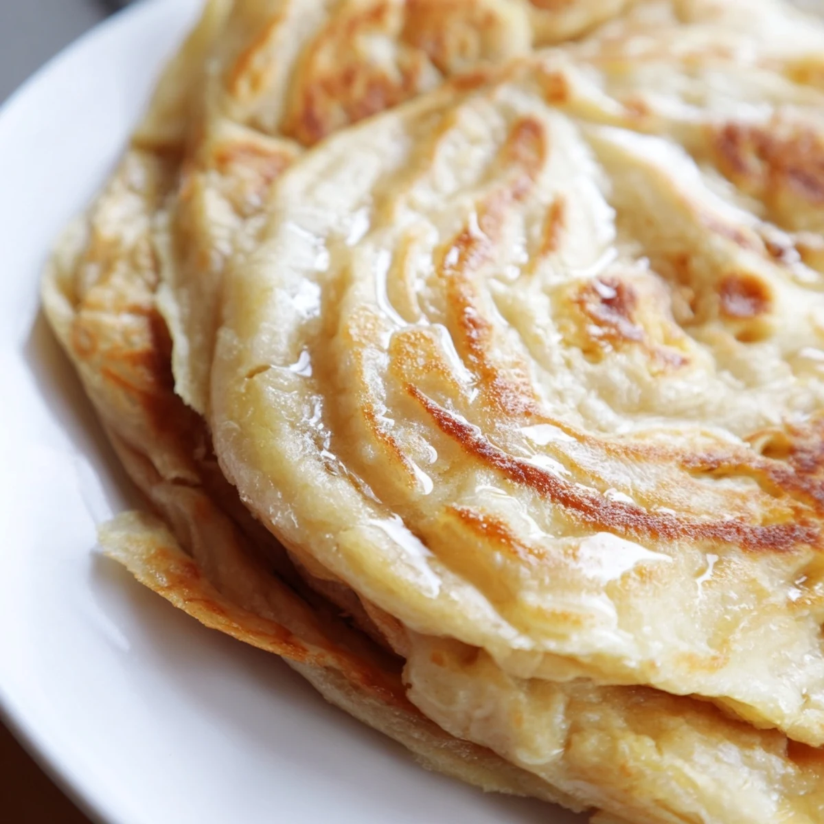 Hand-torn piece of warm roti canai revealing signature flaky interior layers perfect for dipping in curry