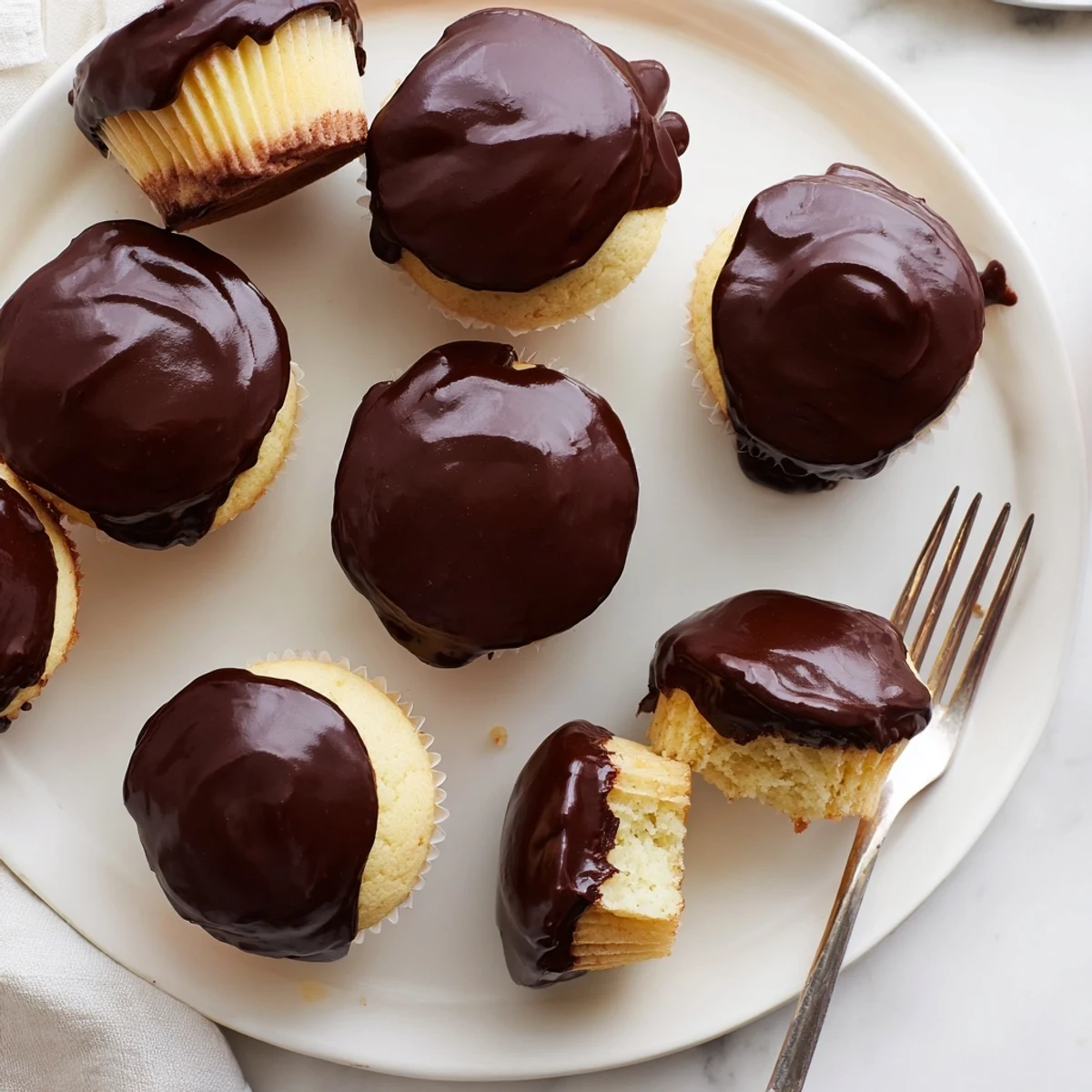 Golden Boston cream pie cupcakes topped with glossy chocolate ganache and filled with creamy vanilla custard