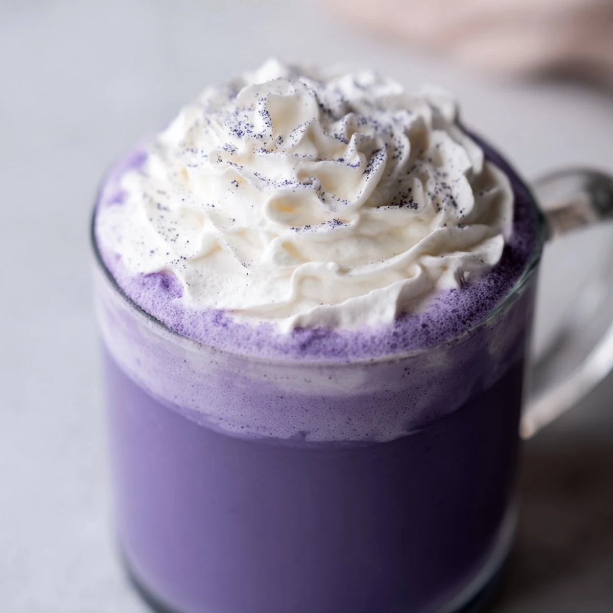Creamy purple ube latte topped with whipped cream in a glass mug