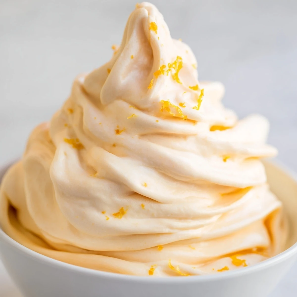 Creamy homemade orange Dole Whip swirled into a tall glass with fresh orange zest sprinkled on top