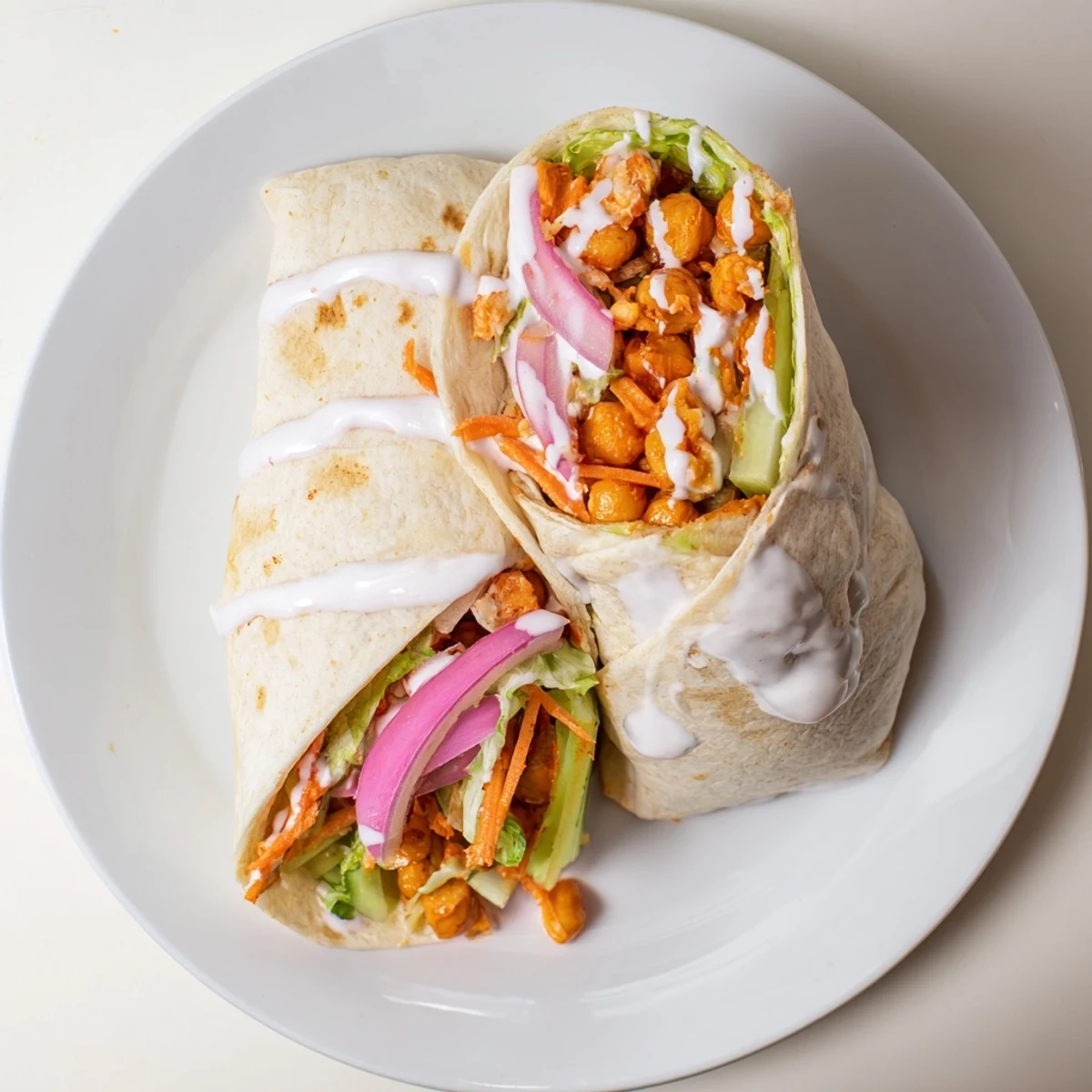 Flour tortilla wrapped around tangy buffalo chickpeas with fresh lettuce, carrots, and celery