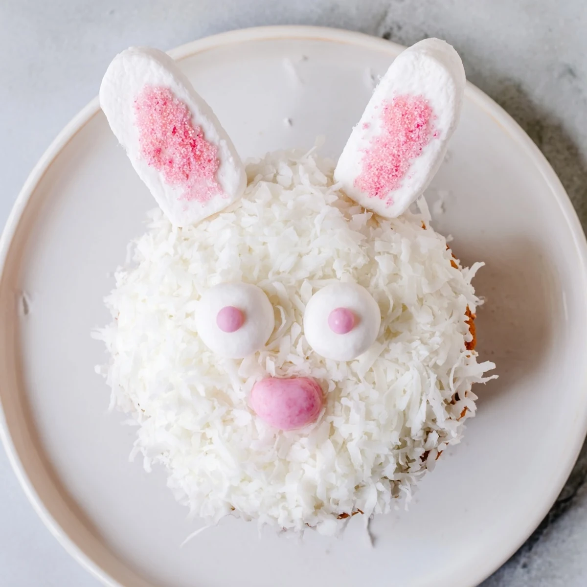 Fluffy vanilla bunny cupcakes topped with coconut fur, pink marshmallow ears, and candy eyes for Easter celebrations