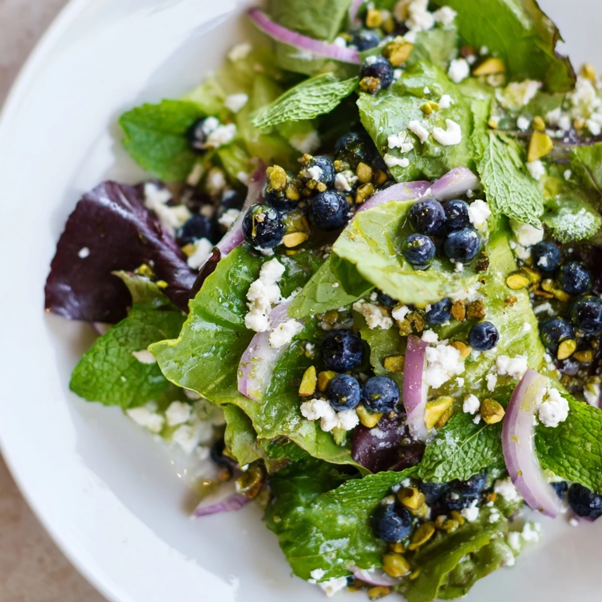 Fresh blueberry pistachio spring salad with vibrant greens, feta, and lemon-honey vinaigrette drizzled over crisp vegetables