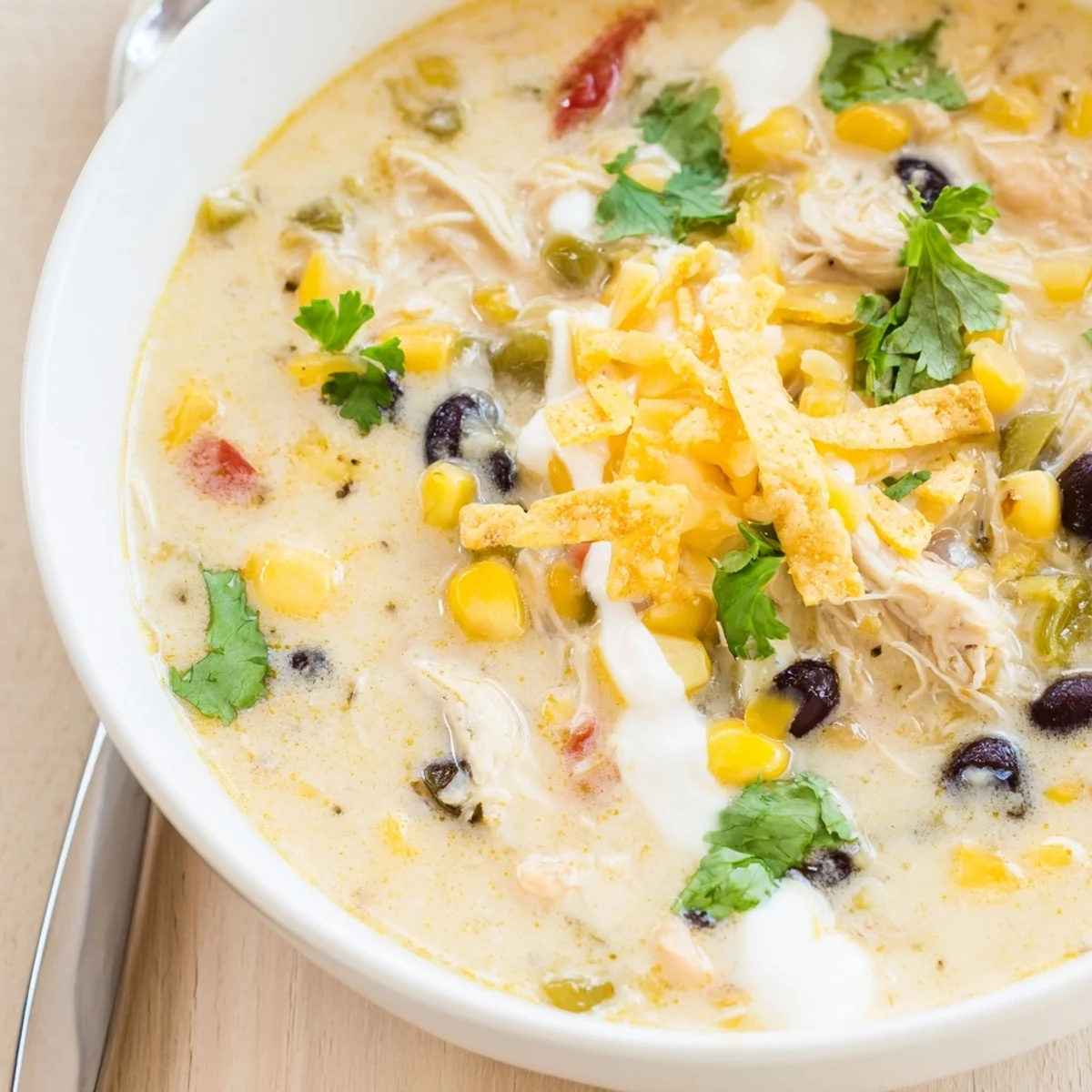 Steaming bowl of easy creamy chicken taco soup topped with crushed tortilla chips, fresh cilantro, and shredded cheddar cheese