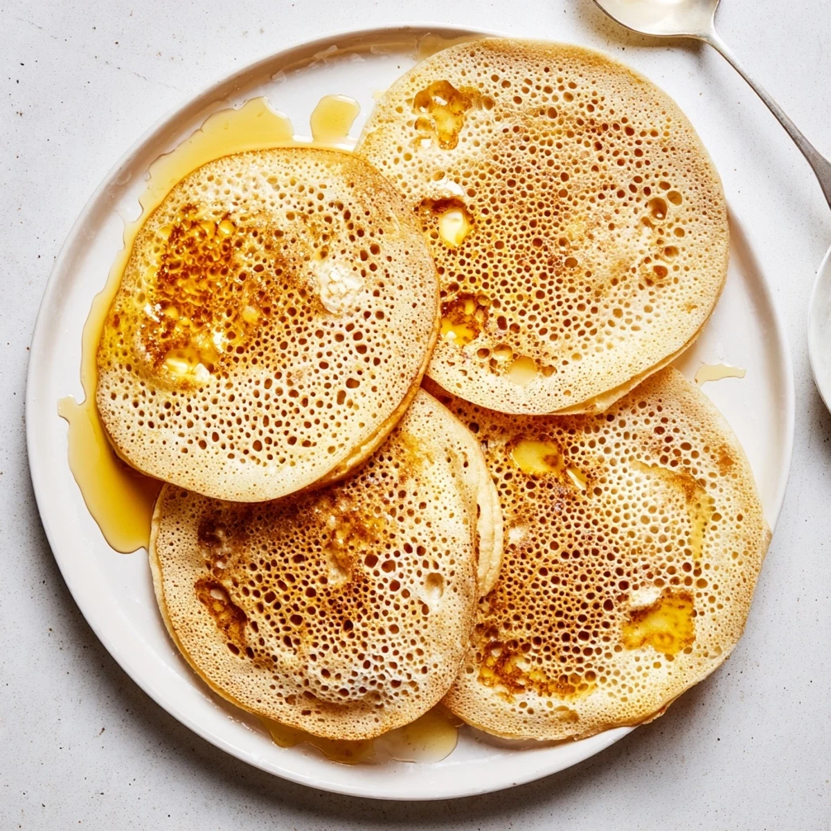 Golden Moroccan Baghrir pancakes sizzling in a skillet with distinctive honeycomb bubble texture