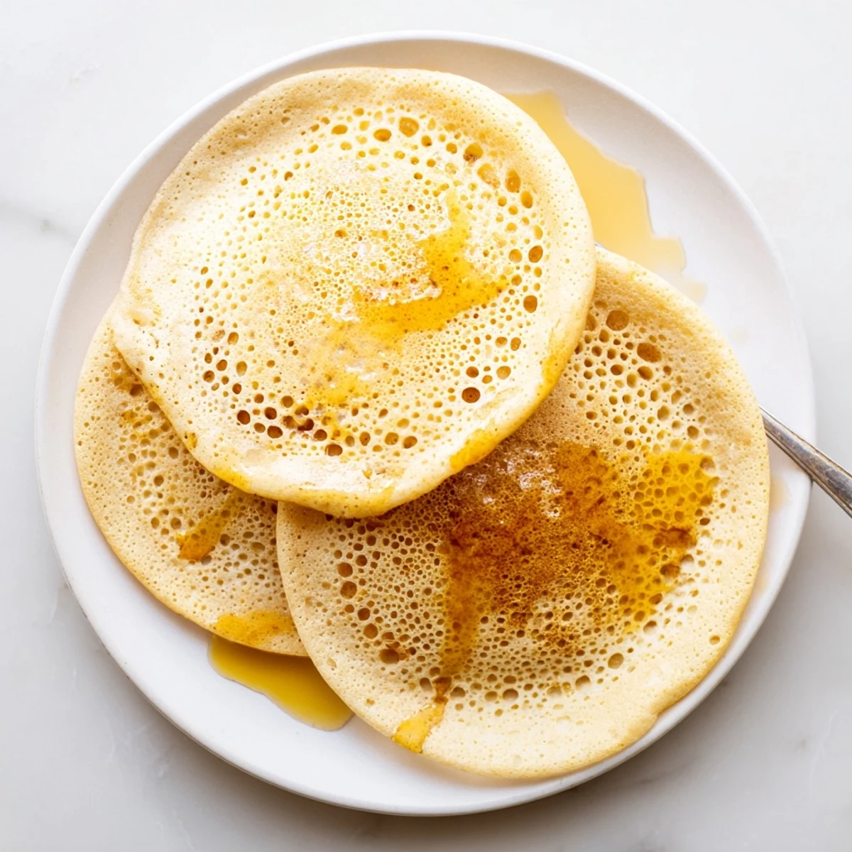 Stack of warm Baghrir Moroccan pancakes drizzled with melted butter and sweet honey