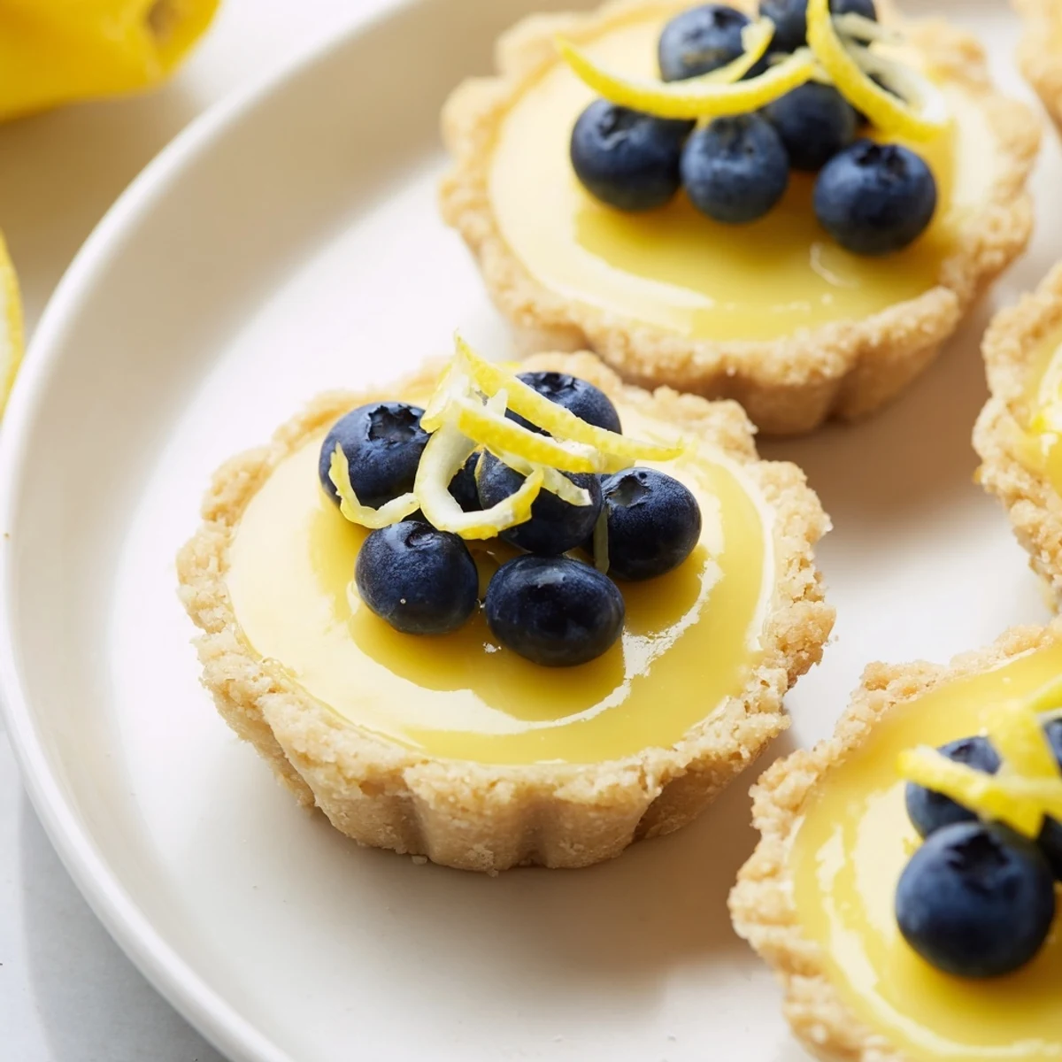 Creamy mini vegan lemon tarts in crisp almond crusts arranged on a serving platter