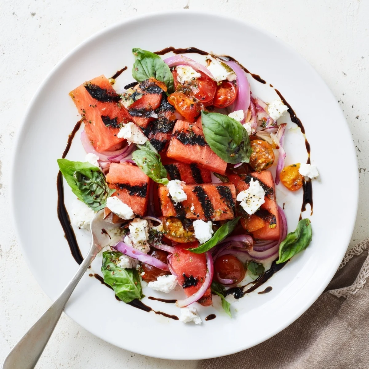 Colorful grilled watermelon feta and basil salad arranged on a white serving platter