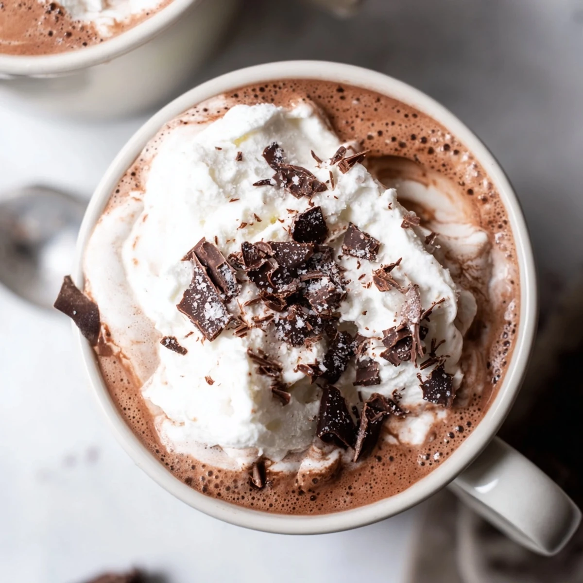 Rich velvety sugar-free creamy keto hot chocolate poured into a white ceramic mug with a metal whisk beside it