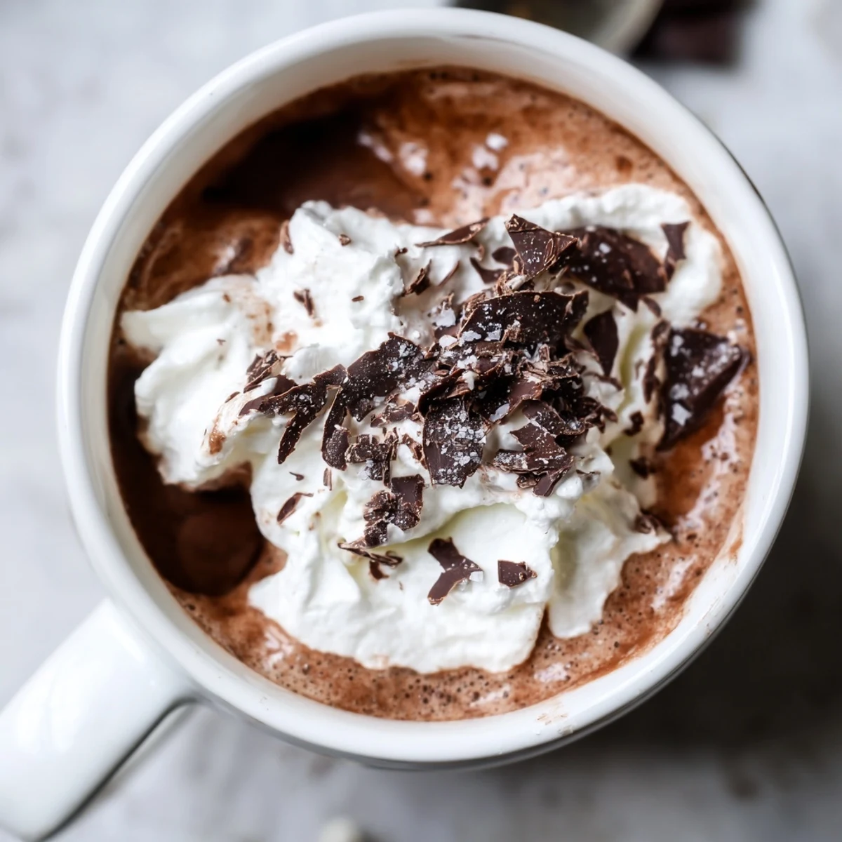 Steamy mug of sugar-free creamy keto hot chocolate topped with whipped cream and shaved dark chocolate