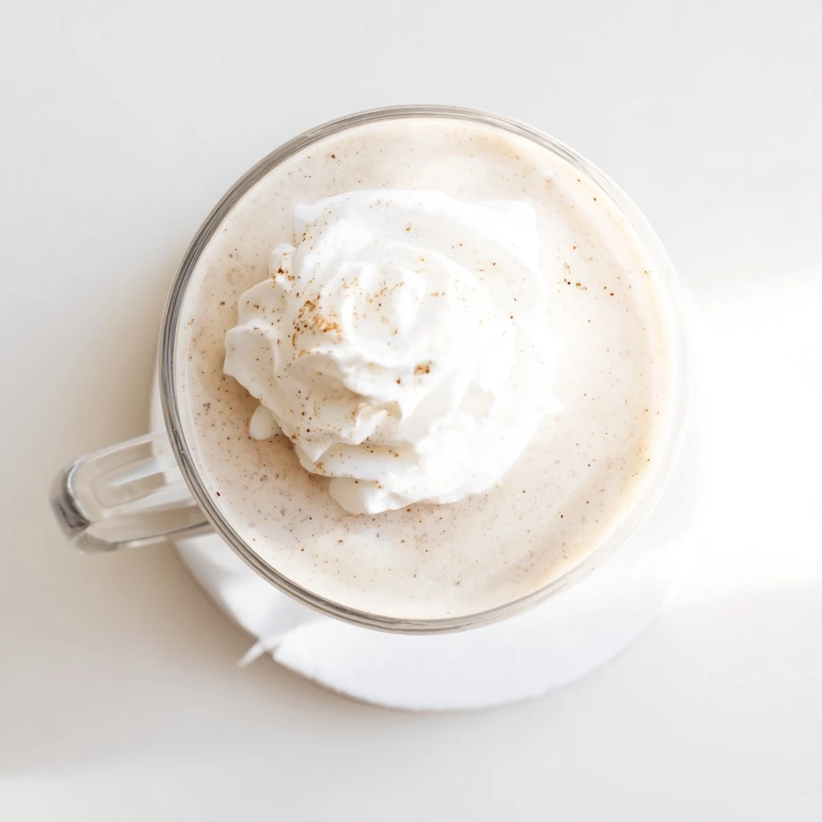 Frothy low-carb eggnog in a clear glass garnished with cinnamon and fresh whipped cream