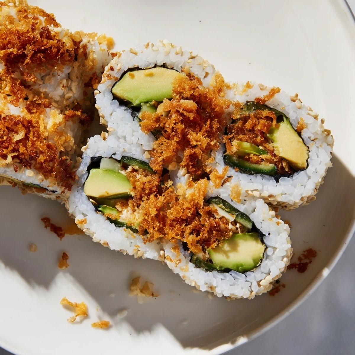 Golden California Crunch Roll Sushi featuring creamy avocado, crab meat, and crispy tempura flakes on a white plate