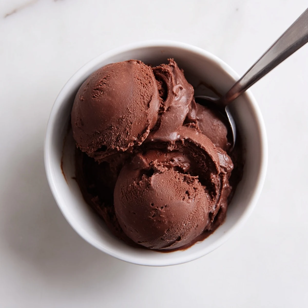 Rich chocolate sourdough ice cream swirling in metal scoop with cocoa dusted background