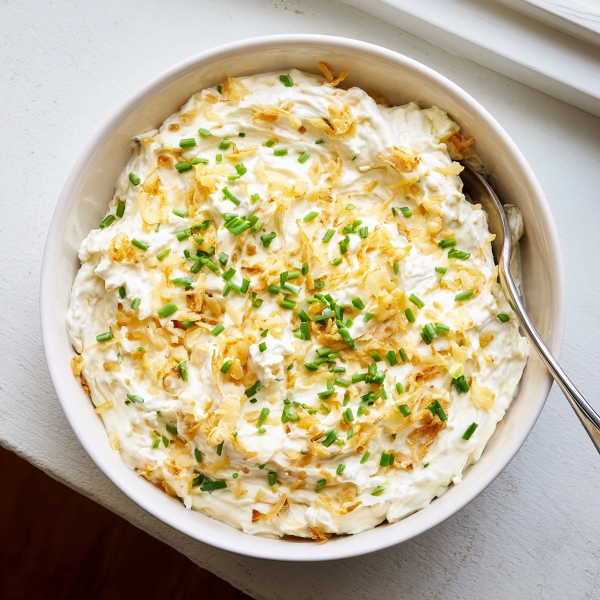 Rich homemade French onion dip served in a white bowl with potato chips