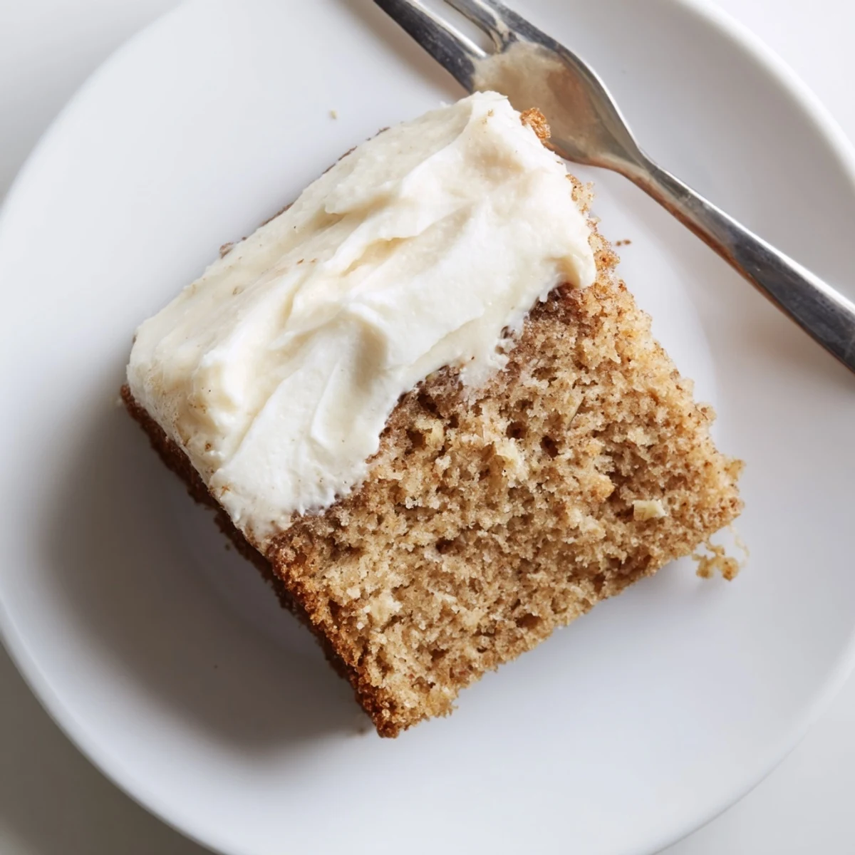 Brown butter banana cake with thick cream cheese frosting spread generously across a moist golden crumb.