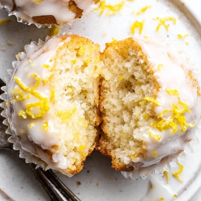 A stack of Glazed Lemon Ginger Muffins with bright zest and steam.