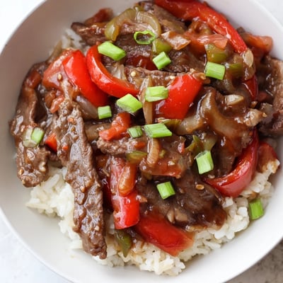 Juicy Slow Cooker Pepper Steak served over fluffy white rice topped with fresh green onions